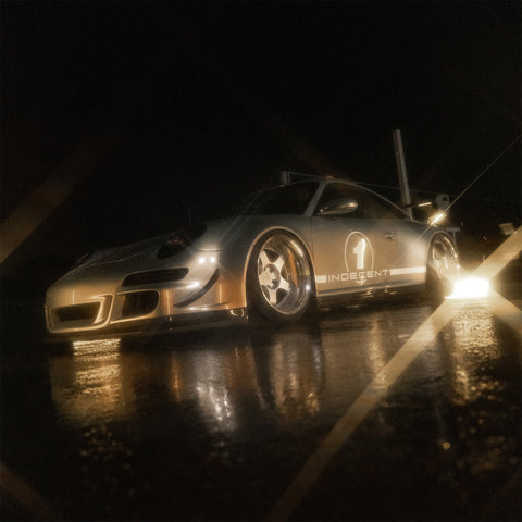 Gold-coloured sports car photographed at night with star-shaped highlights and reflections on the ground