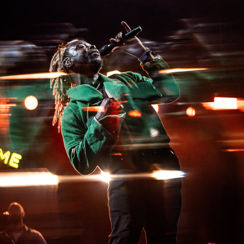 Singer in a green jacket holding a microphone amid Supernova II stage-light streaks
